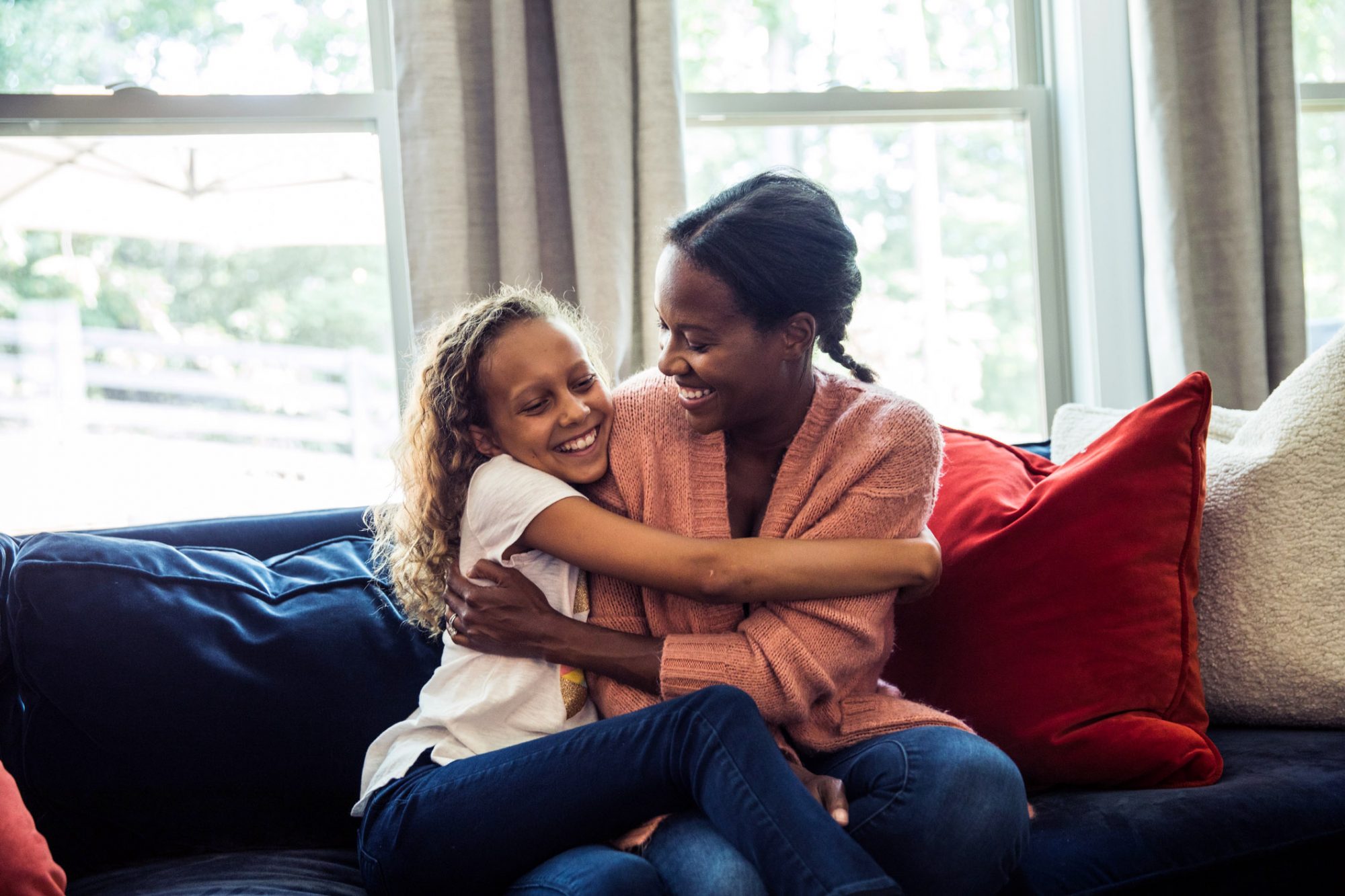 An image of a mom and daughter hugging on a couch.